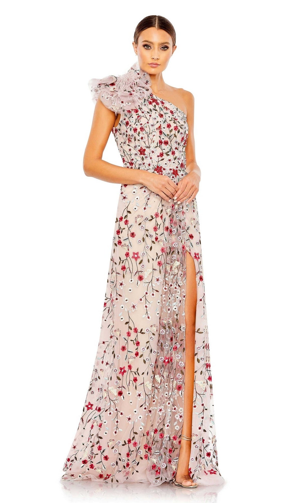 A woman stands against a plain white background wearing the Mac Duggal 20331 One-Shoulder Print Formal Gown, featuring floral embroidery, a ruffled shoulder detail, and a high leg slit.